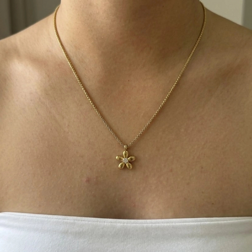 Gold necklace with a flower pendant worn by a person on a plain background