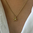 Gold flower necklace on a person wearing a white top