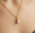 Gold necklace with a teardrop-shaped diamond pendant on a person's neck.