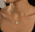 Gold necklace with a round, diamond-studded pendant on a person's neck.