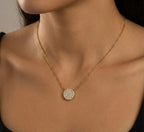 Gold necklace with a round, diamond-studded pendant on a person's neck.