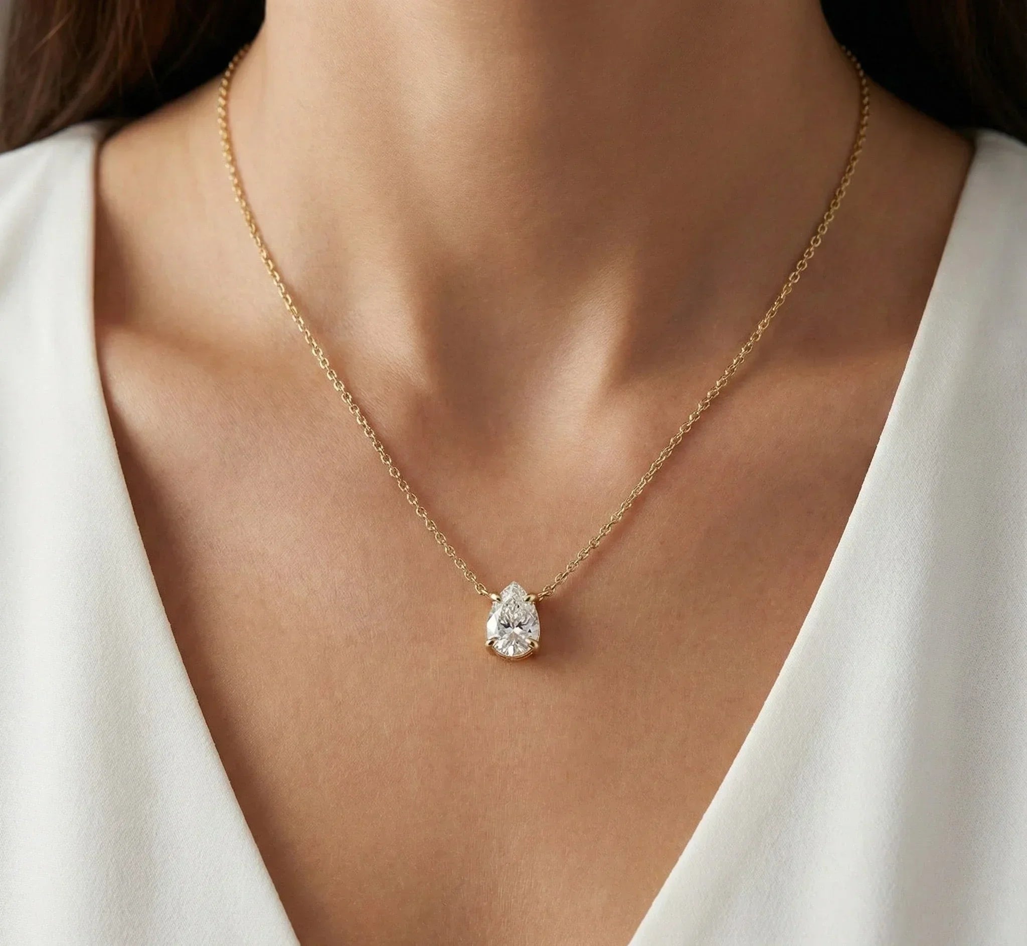 Gold necklace with a diamond pendant worn by a person in a white outfit.