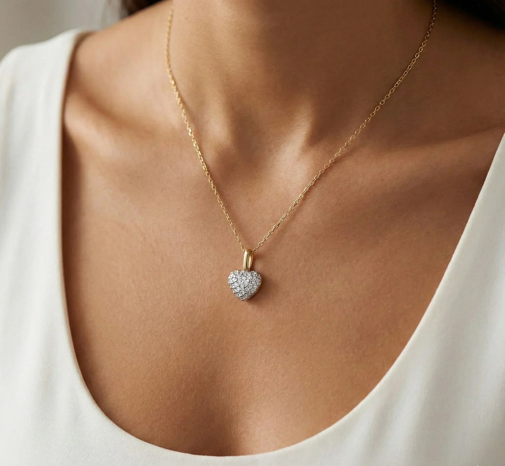 Gold necklace with a heart-shaped diamond pendant on a person wearing a white top.