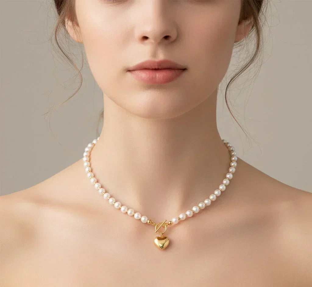 Pearl necklace with a gold heart pendant worn by a model against a neutral background