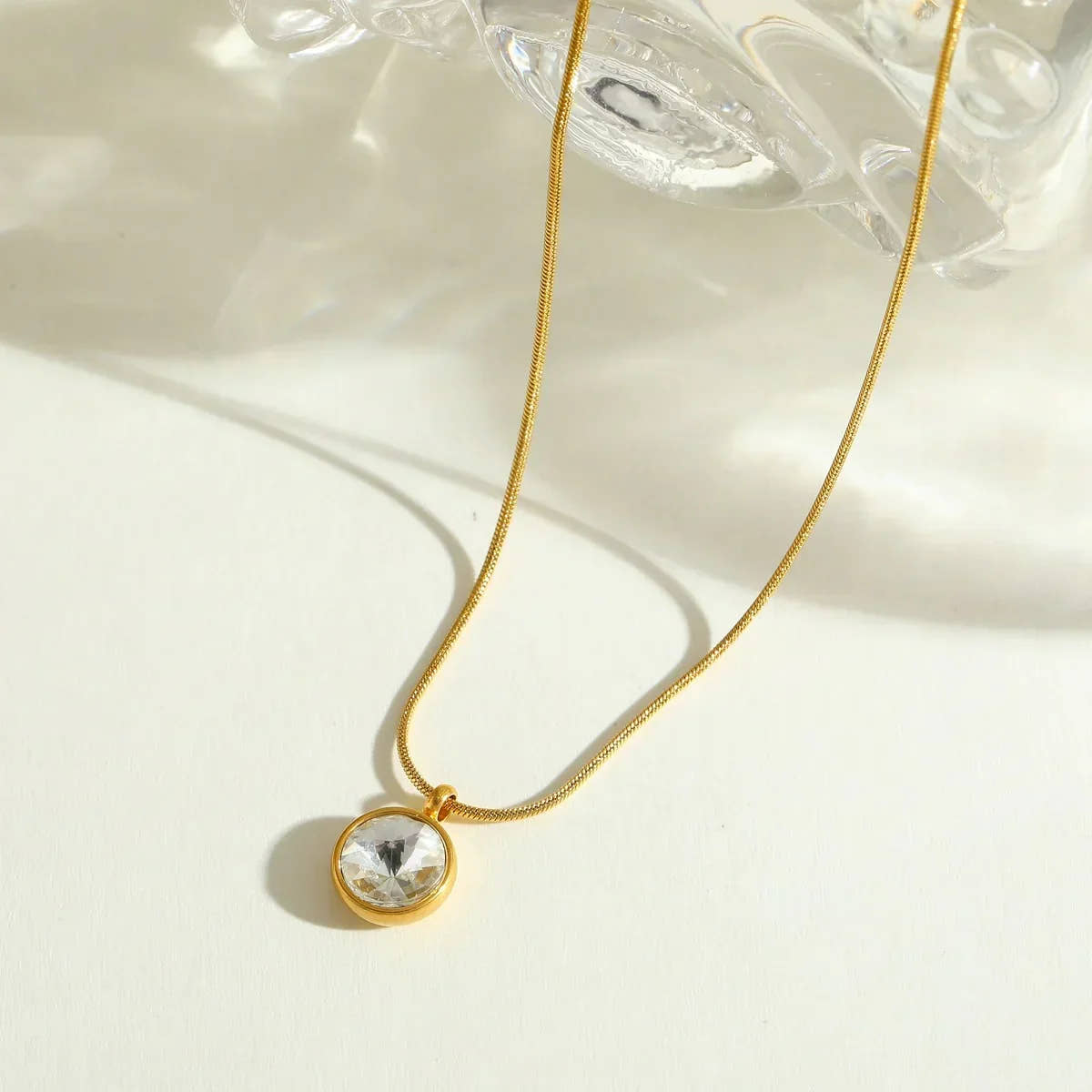 Gold necklace with a clear pendant on a light background