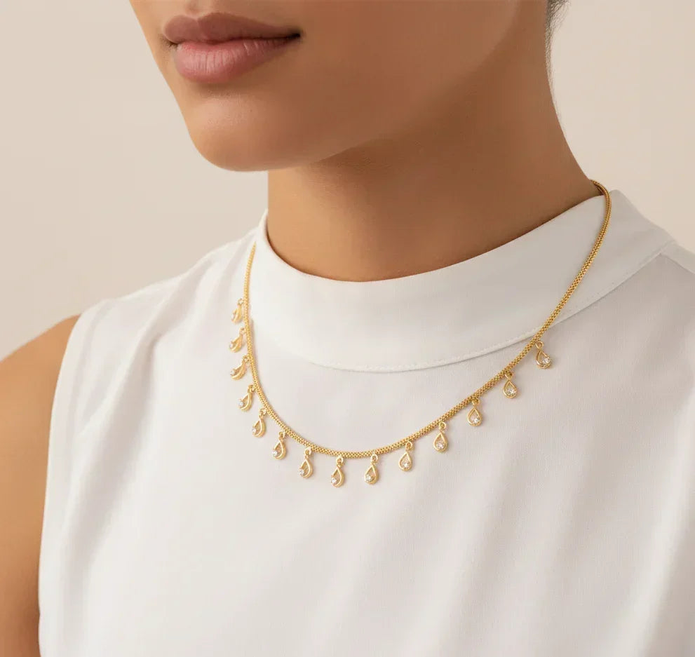 Gold necklace with teardrop pendants worn by a person in a white top against a neutral background