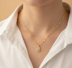 Gold necklace with a pendant on a mannequin wearing a white shirt against a beige background