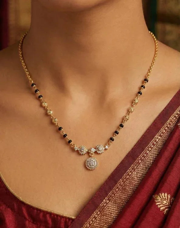 Necklace with black and gold beads worn by a person in a maroon saree.