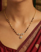 Necklace with black and gold beads worn by a person in a maroon saree.
