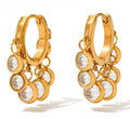 Gold hoop earrings with circular designs and clear stones on a white background