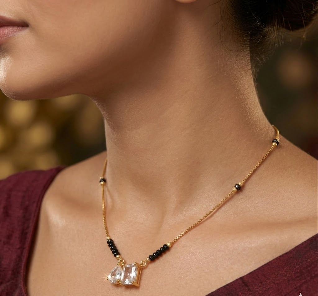 Close-up of a woman wearing a gold necklace with black beads and a clear pendant.